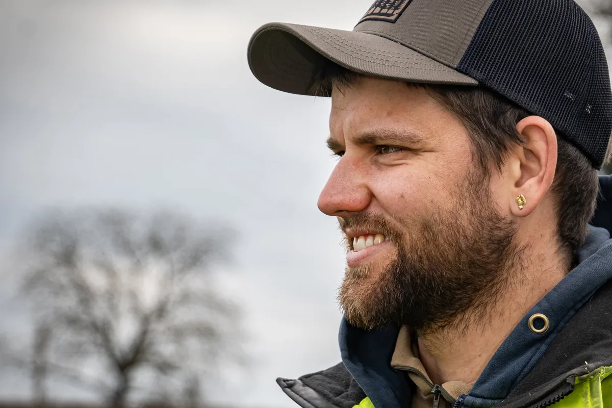 «Es geht nicht nur darum, den Humus zu regenerieren, sondern auch das bäuerliche Einkommen»: Benjamin Denzler ist von der regenerativen Landwirtschaft überzeugt. Porträtbild von Benjamin Denzler von der Seite. Man sieht einen bärtigen jungen Mann mit Baseballmütze und goldenem Ohrstecker von der Seite.